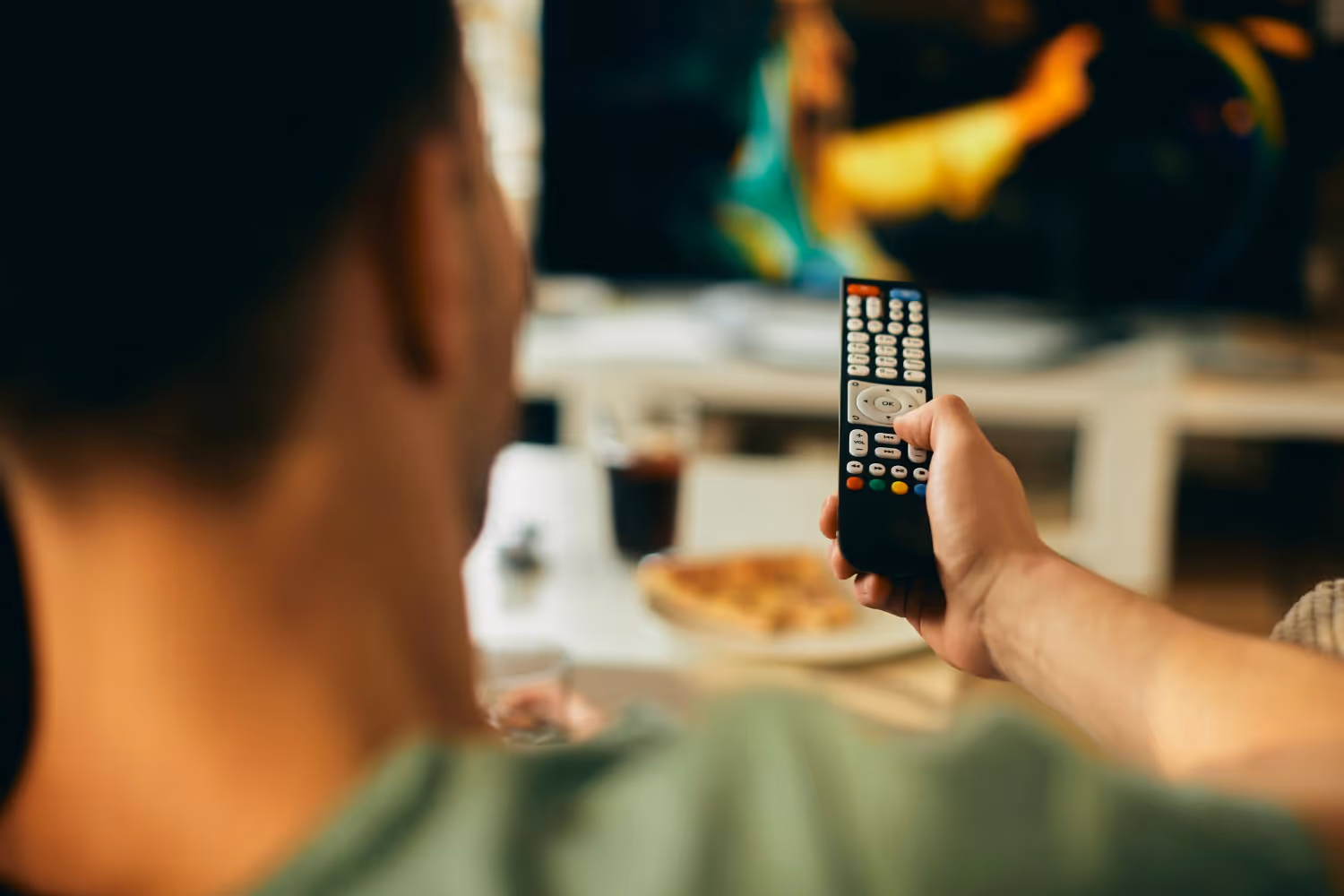 mężczyzna trzymający pilot tv w ręku siedzący na kanapie przed tv