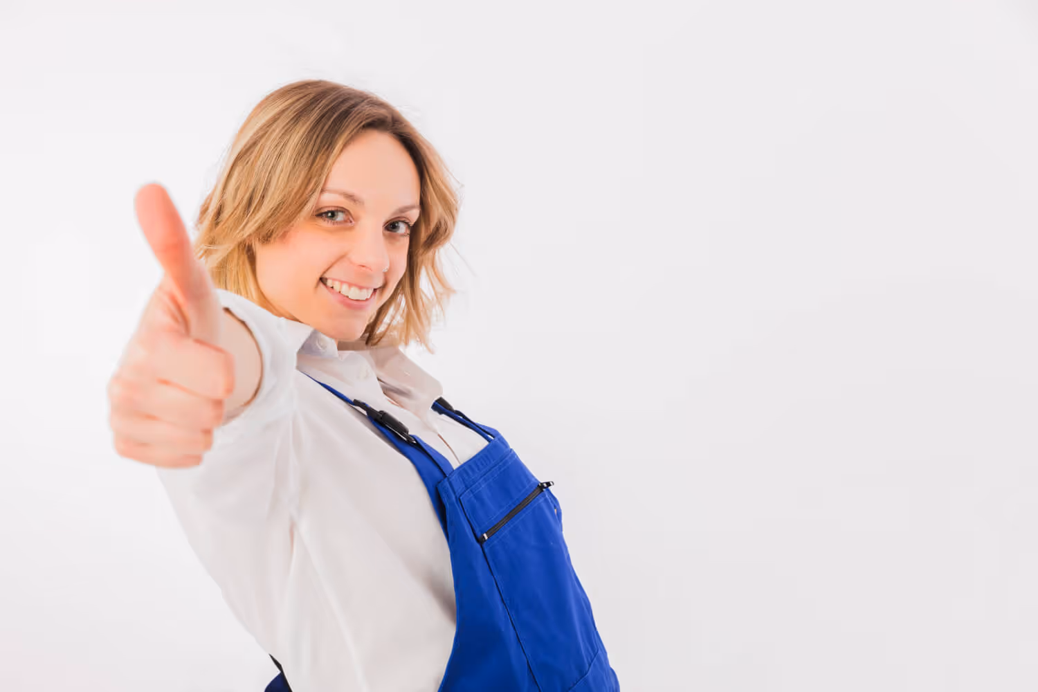 Smiling woman in blue apron giving a thumbs-up against a white background.