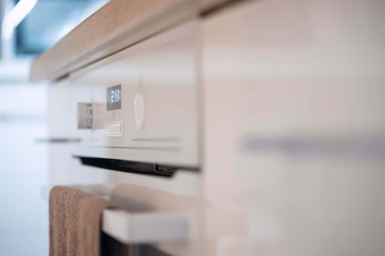 Close-up of a white kitchen oven with a digital display showing 23:51 and a brown towel hanging from the handle.