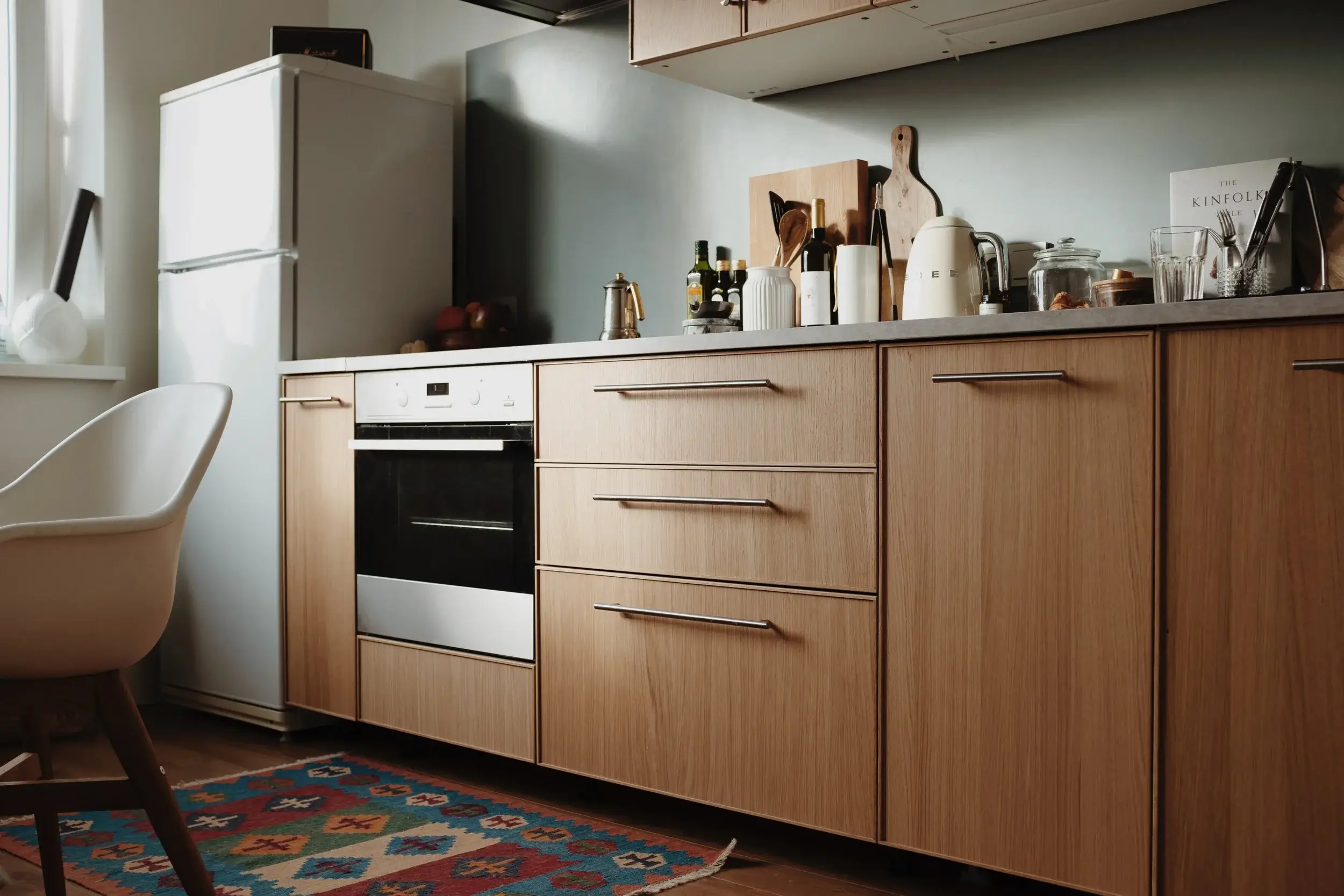 Modern kitchen interior with wooden cabinets, a built-in oven, white refrigerator, and colorful patterned rug.